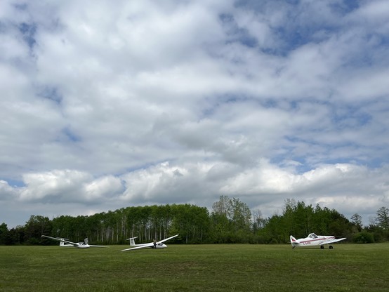 Gliders on a grass field under a mostly cloudy sky