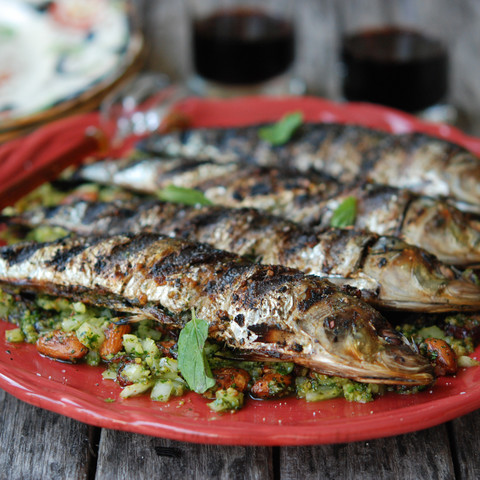 Grilled sardines rest on a bed of tomatoes and greens on a tomato-red plate