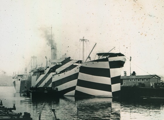 The USS West Mahomet appears at anchor in dazzle camouflage in 1918.  Large bands of dark and white are painted across it in intersecting patterns.